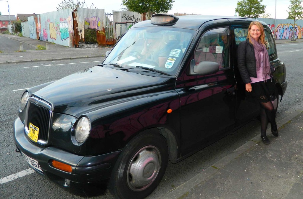 Mulher posa para foto com um tradicional táxi preto britânicos em rua de Belfast, na Irlanda do Norte