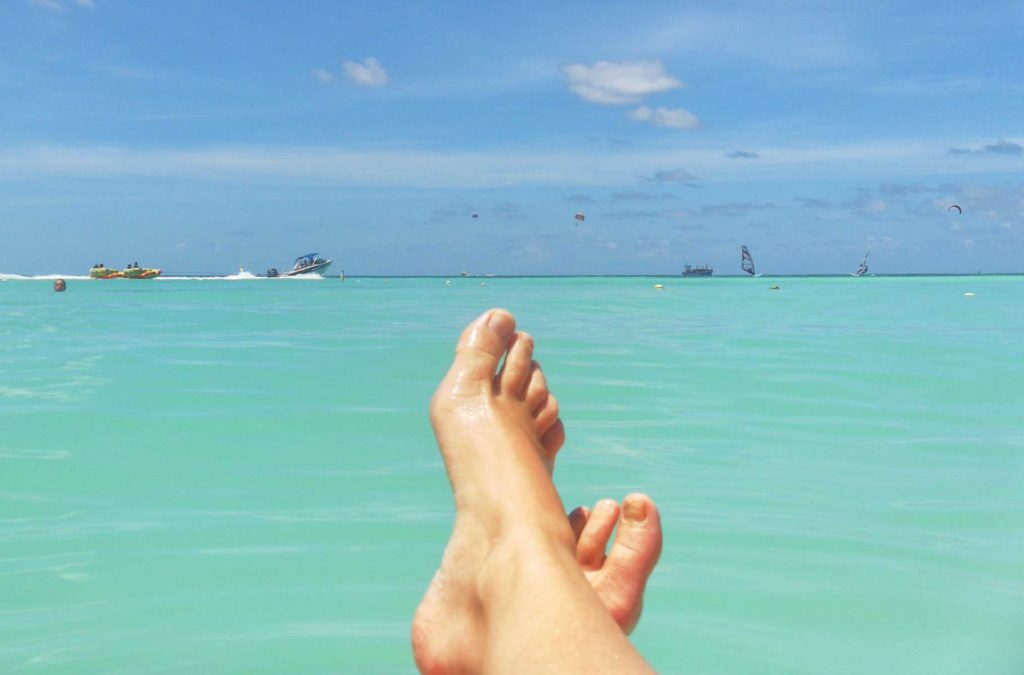 Pessoa cruza os pés de frente para o mar em praia de Aruba