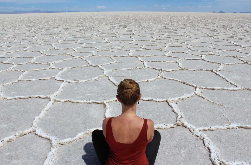 Mulher posa para foto sentada no chão branco do Salar do Uyuni, na Bolívia