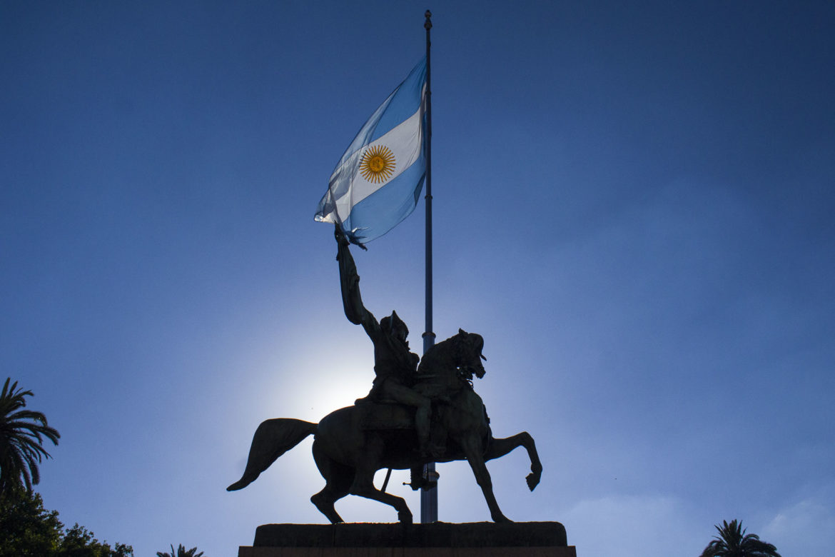 Monumento e bandeira contra o sol e o céu azul na Plaza de Mayo, em Buenos Aires (Argentina)