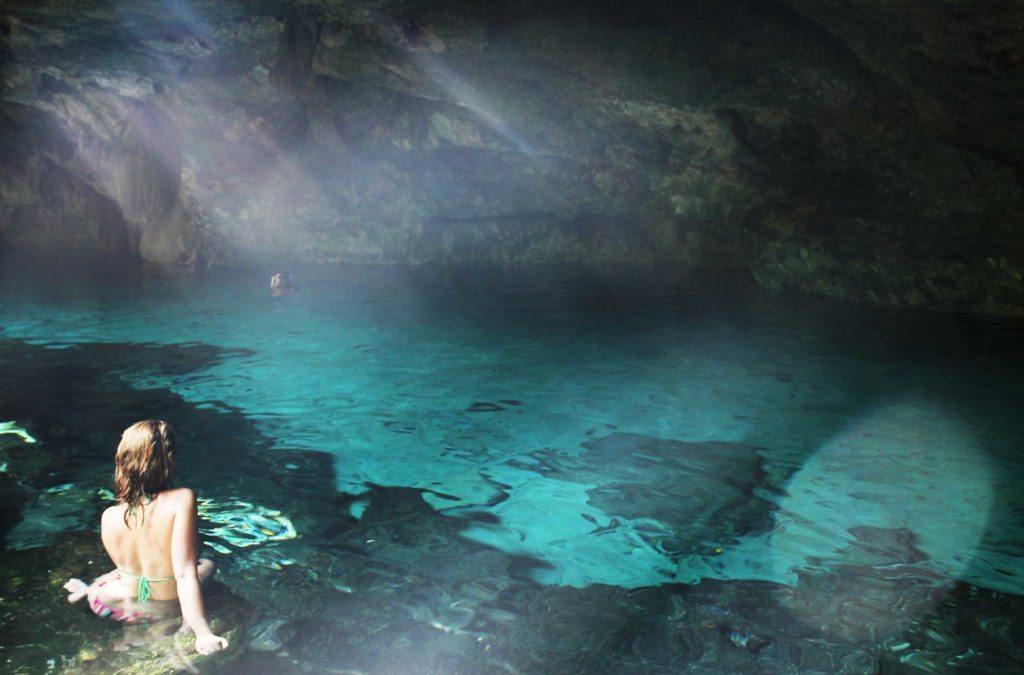Mulher senta nas rochas dentro do Cenote Dos Ojos, o mais famoso do México