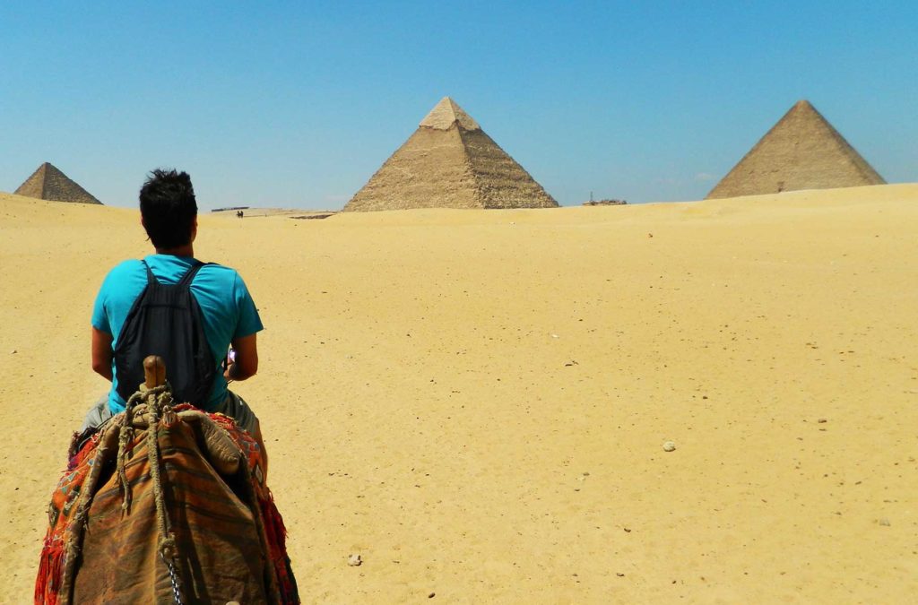Turista se aproxima das Pirâmides de Gizé (Egito) montado em um camelo