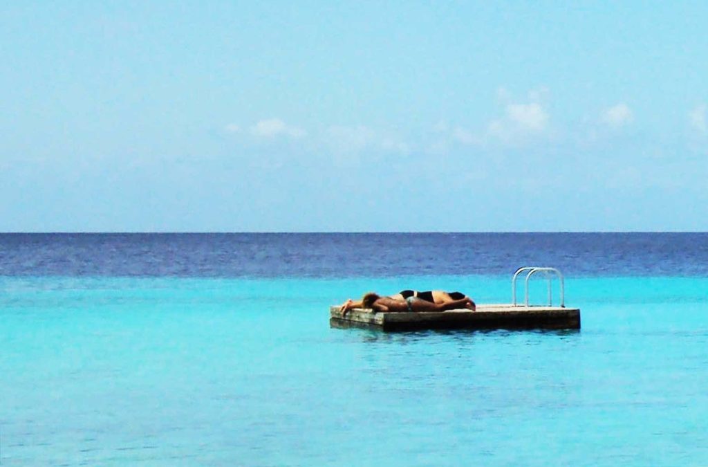 Casal toma sol em plataforma que flutua no mar na Praia de Cas Abao, em Curaçao