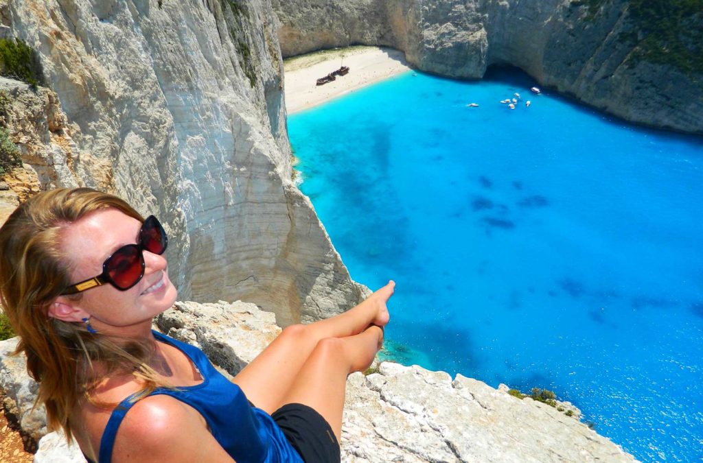 Mulher posa para foto na beira dos penhascos sobre a Praia de Navagio, na Grécia