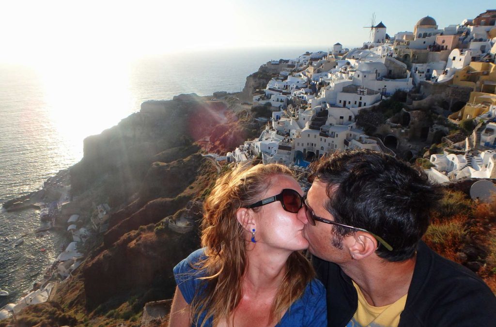 Casal se beija no vilarejo de Oía, em Santorini, com o pôr do sol no mar ao fundo