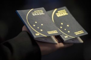 Mão de homem segura dois passaportes brasileiros contra um fundo preto