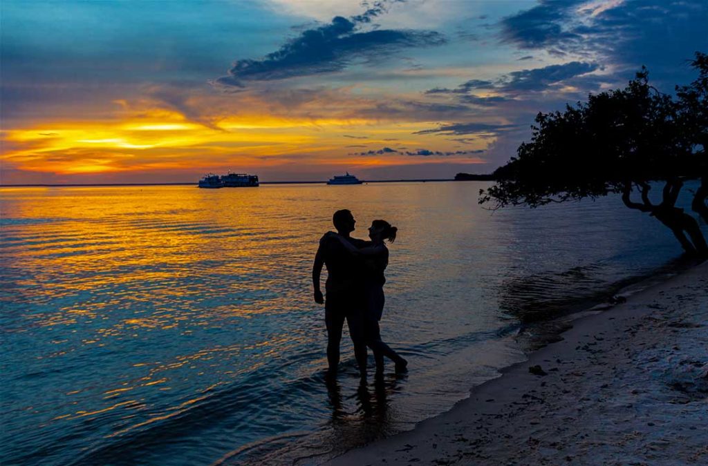 Casal se abraça ao pôr do sol na beira da praia na Ilha do Amor, em Alter do Chão (PA)