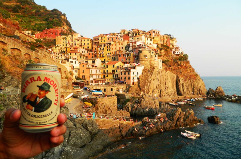Mão segura lata de cerveja com a vista de Cinque Terre, na Itália, ao fundo