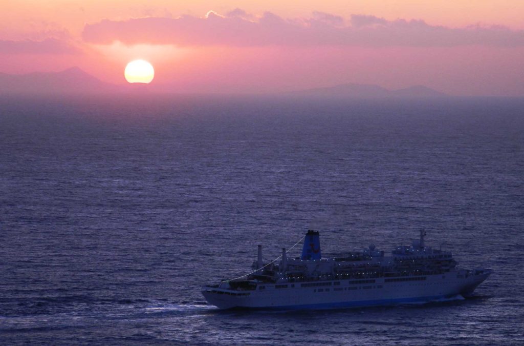 Navio navega ao pôr do sol na vila de Oía, em Santorini (Grécia)