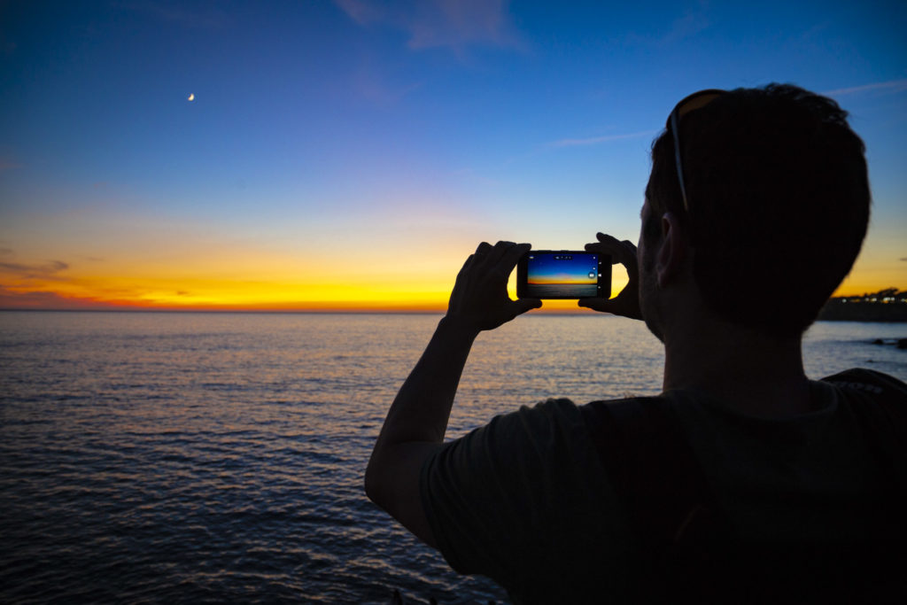 Homem tira foto do anoitecer no mar em Cascais, Portugal