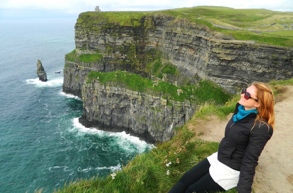 Mulher posa para foto sentada na beira dos Cliffs of Moher, na Irlanda