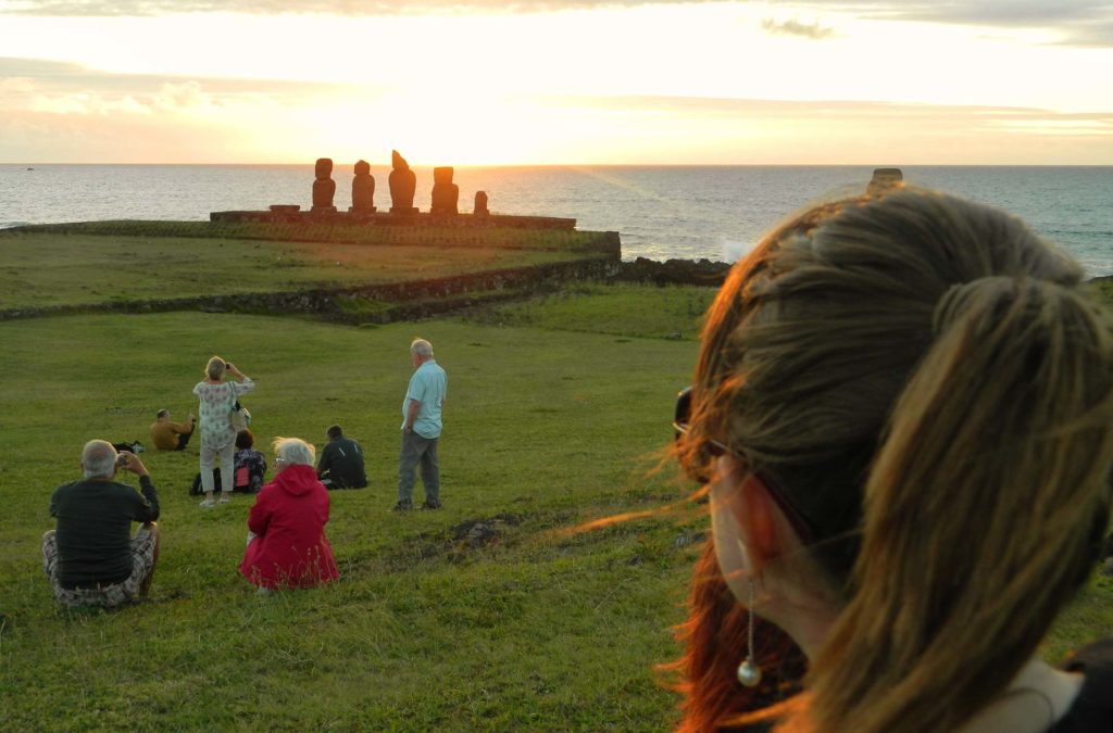 Mulher admira o pôr do sol na Ilha de Páscoa com moais ao fundo