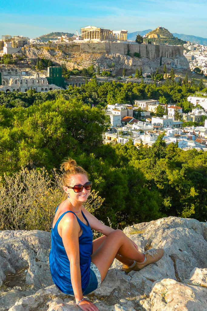 Mulher posa para foto na Colina Philopappos, com a Acrópole de Atenas ao fundo