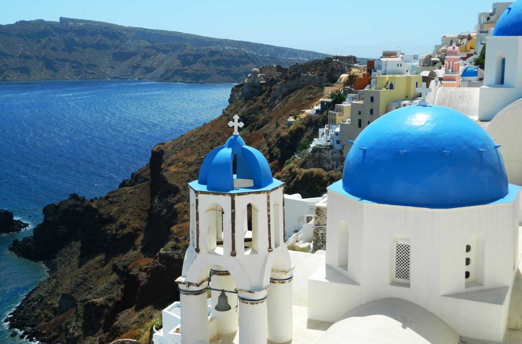 Igreja branca com domos azuis sobre os penhascos da vila de Oía, em Santorini (Grécia)