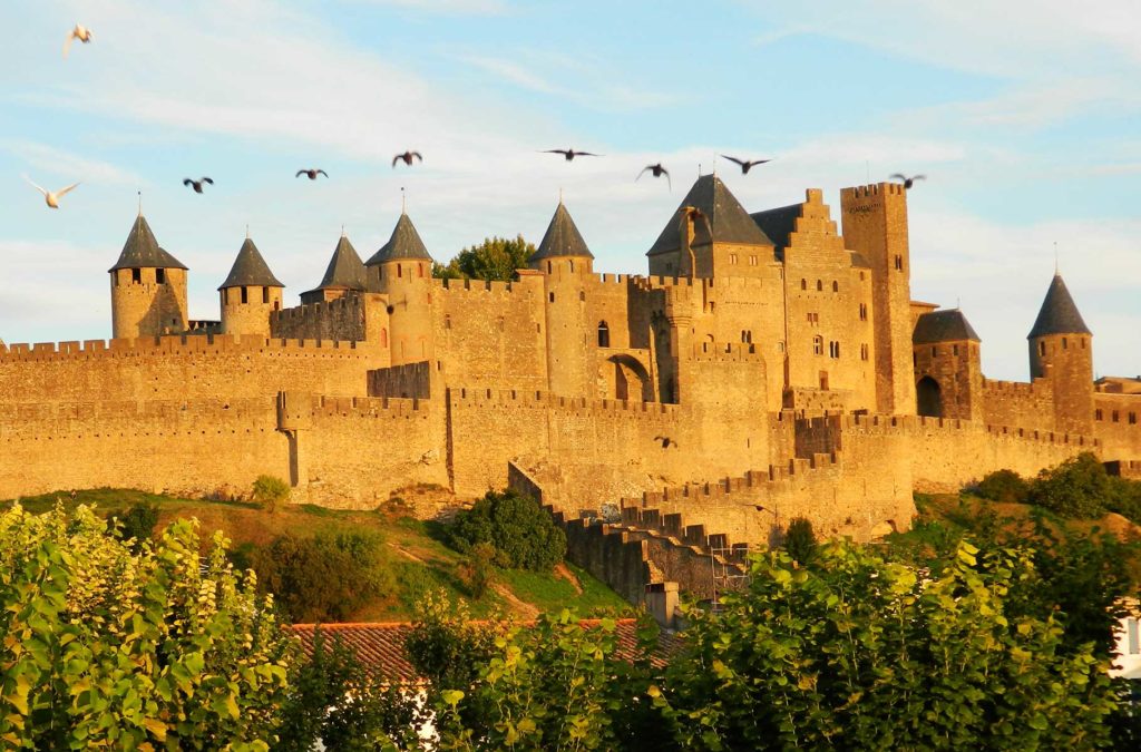 Pássaros voam sobre a cidade medieval de Carcassonne, vista desde a Pont Vieux, ao entardecer
