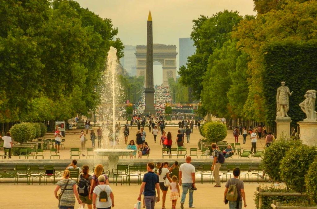 Pessoas caminham pelo Jardim das Tuileries, em Paris, com o Obelisco e o Arco do Triunfo ao fundo