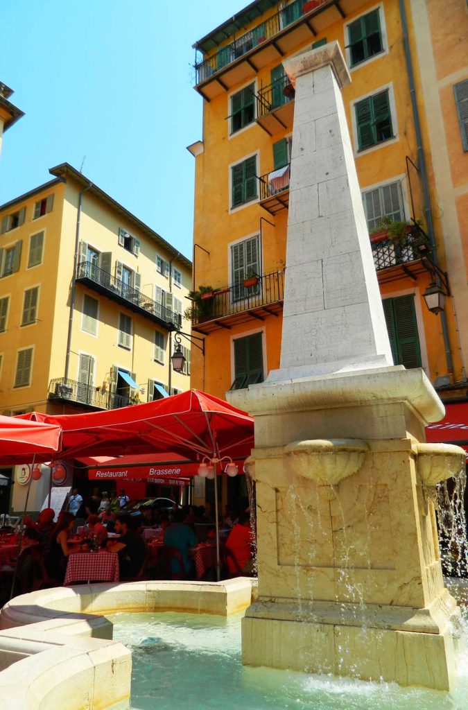 Fonte cercada de mesas de restaurantes na Place Rossetti, em Nice