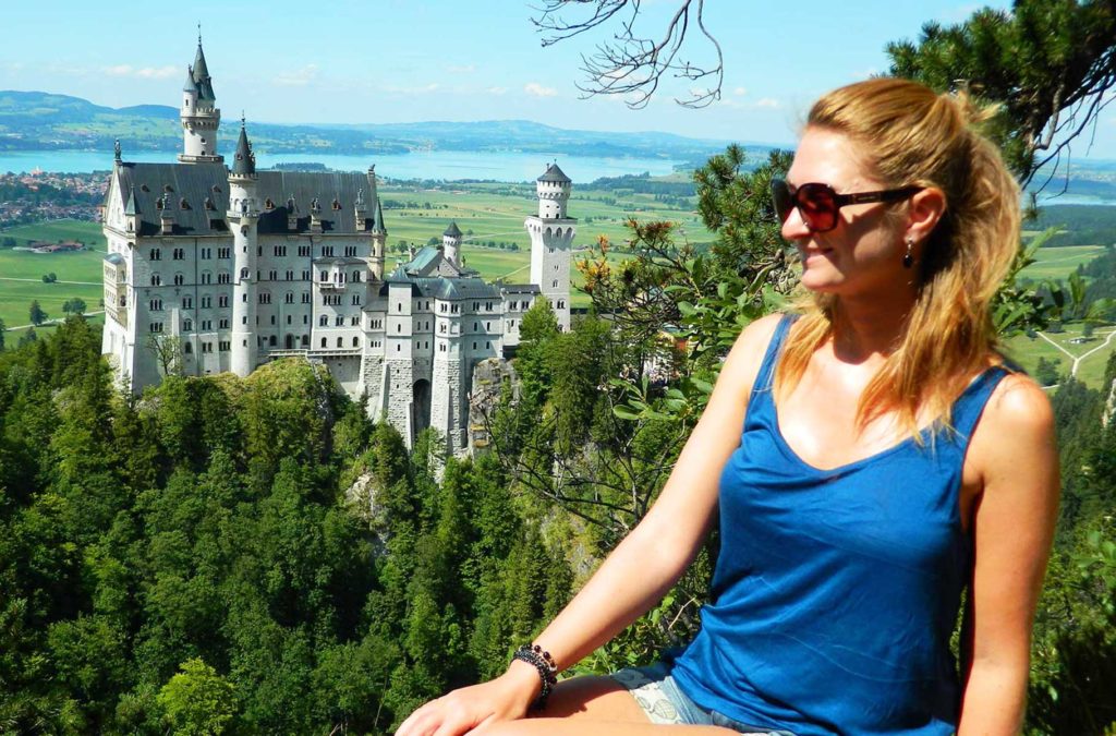 Turista posa para foto com o Castelo de Neuschwanstein ao fundo