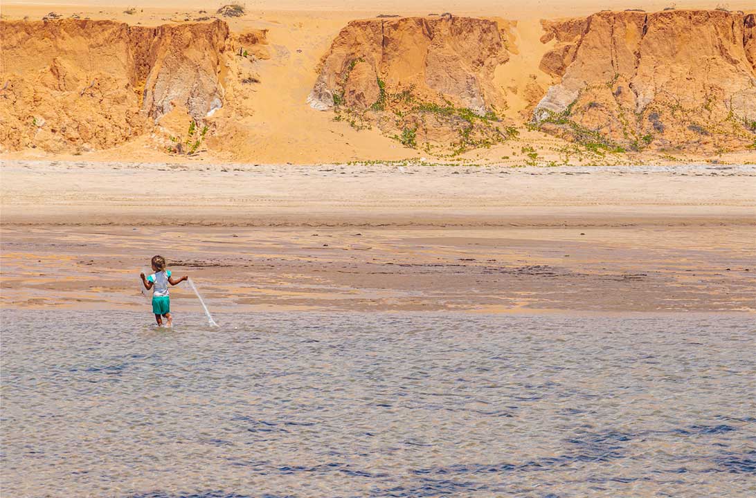 Menina brinca com rede de pesca na Praia de Canoa Quebrada, no Ceará (Brasil)