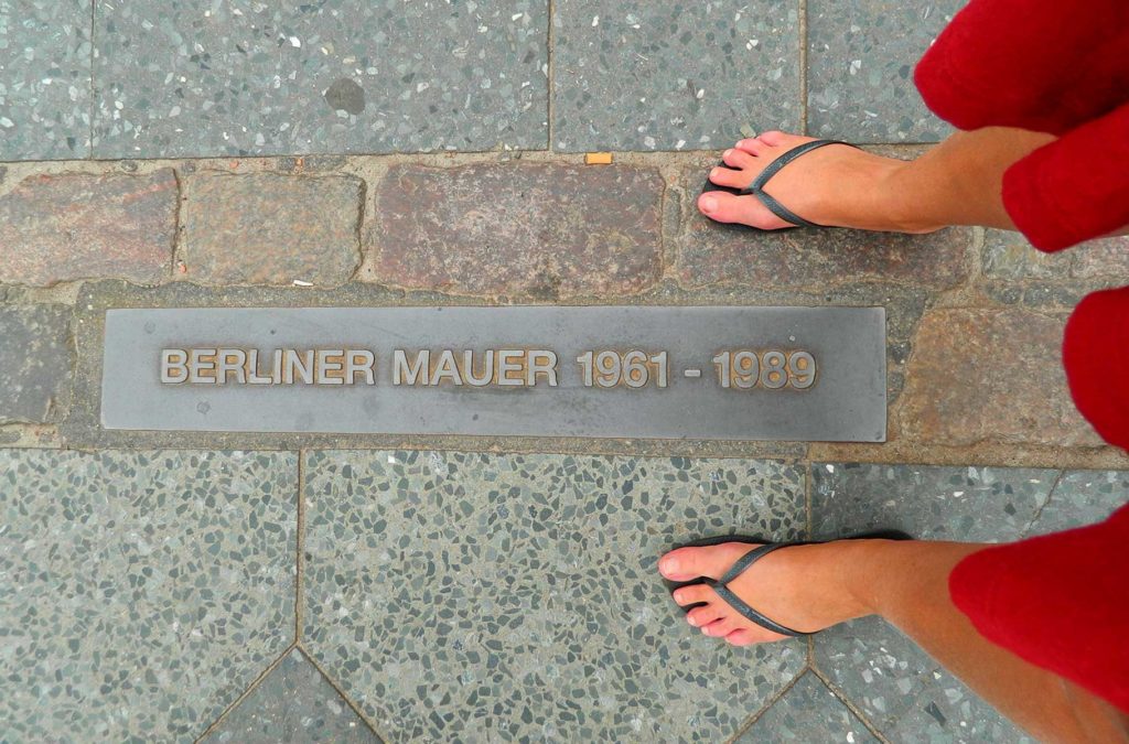 Turista tira foto com os pés sobre a linha onde se erguia o Muro de Berlim