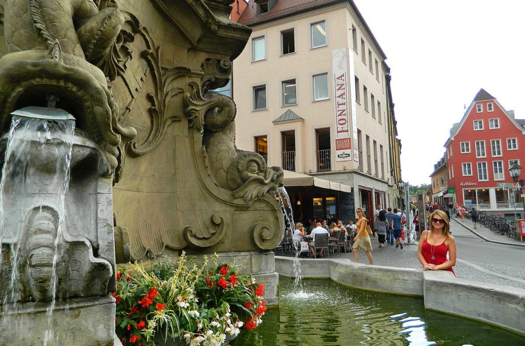 Turista posa para foto na Fonte dos Quatro Tubos, em Würzburg