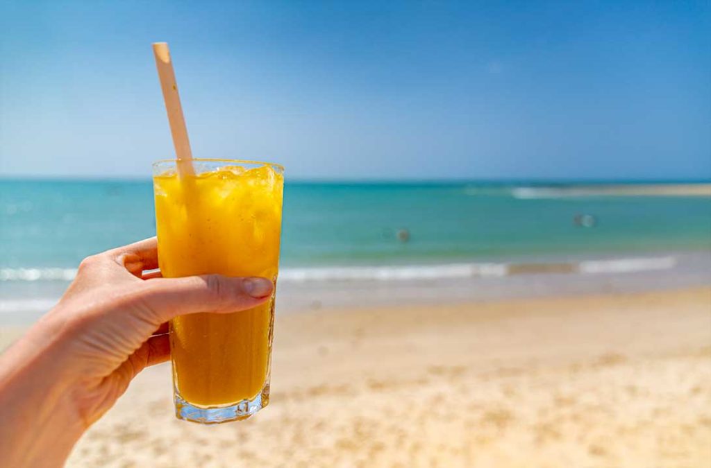 Turista segura caipirinha do Bar Nativus com a praia ao fundo