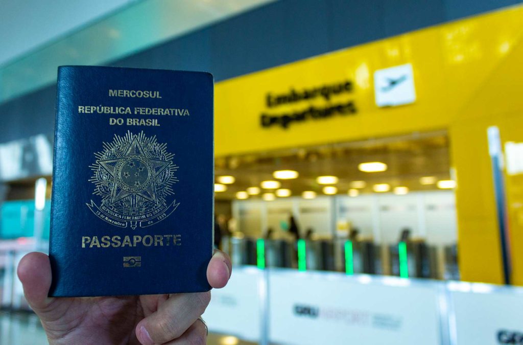 Turista segura passaporte brasileiro em frente ao portão de embarque internacional de aeroporto