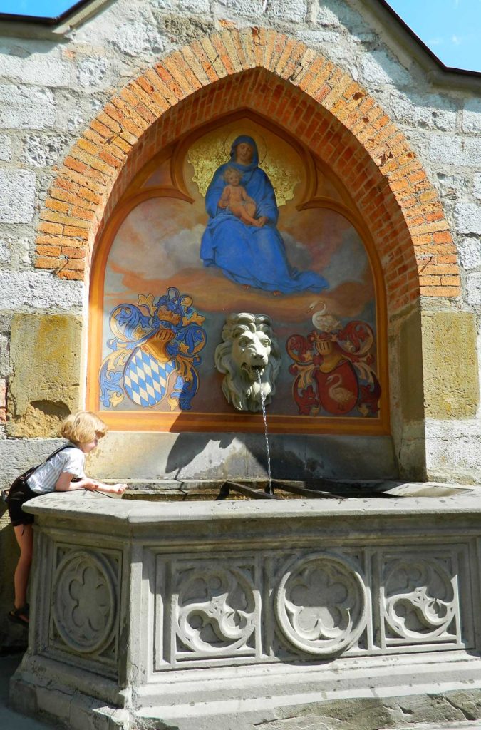 Criança brinca em fonte no pátio do Castelo de Hohenschwangau