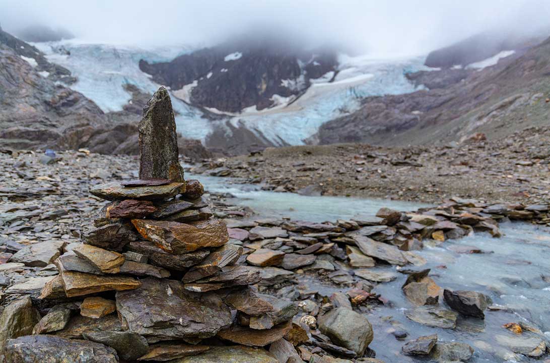 Montes de pedras deixados por turistas são emoldurados pelo Glaciar Vinciguerra ao fundo
