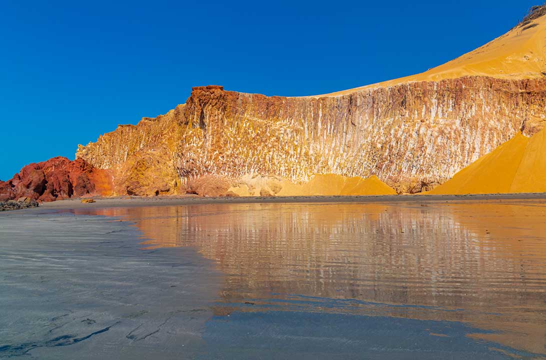 Falésias da Praia de Ponta Grossa refletem na areia banhada pelo mar