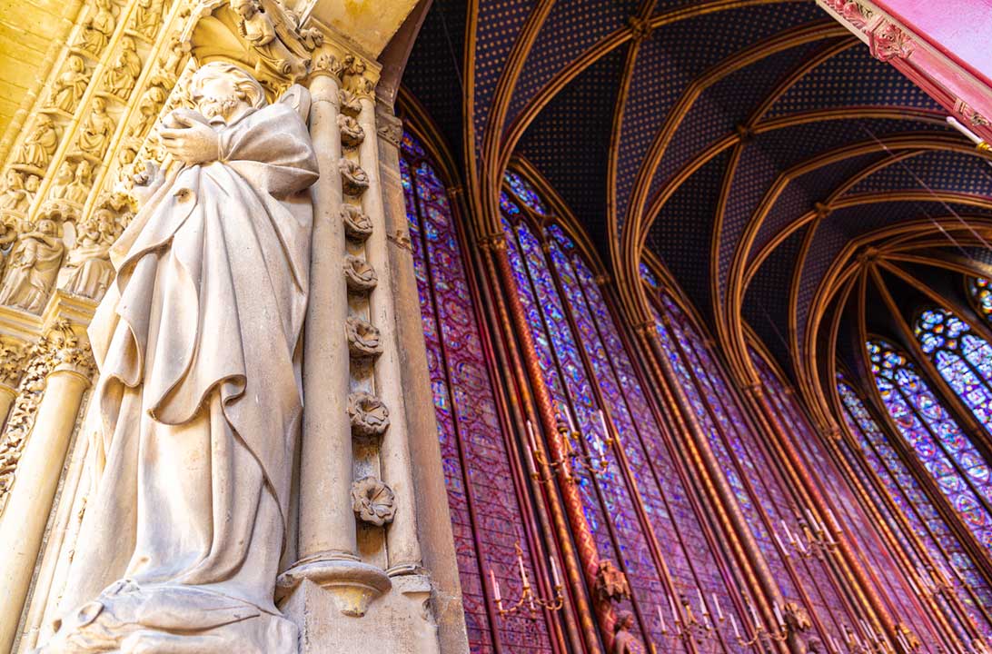 Estátua em frente à entrada da Sainte-Chapelle, em Paris, com os vitrais góticos ao fundo