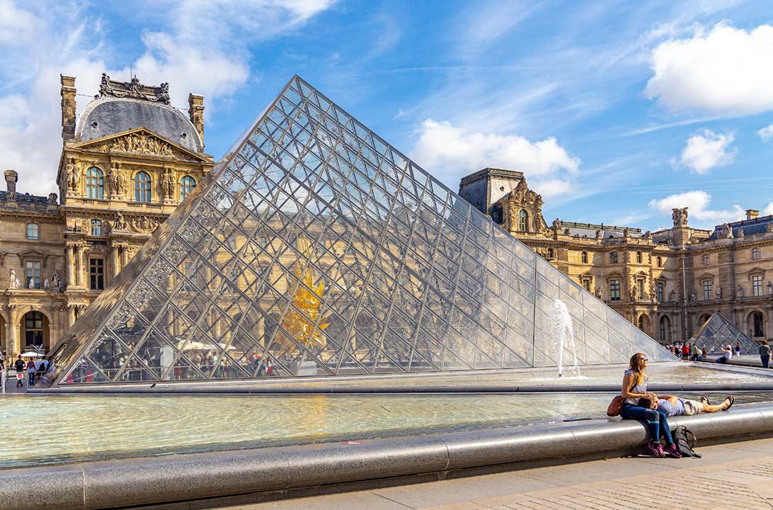 Casal descansa na Pirâmide do Museu do Louvre, em Paris
