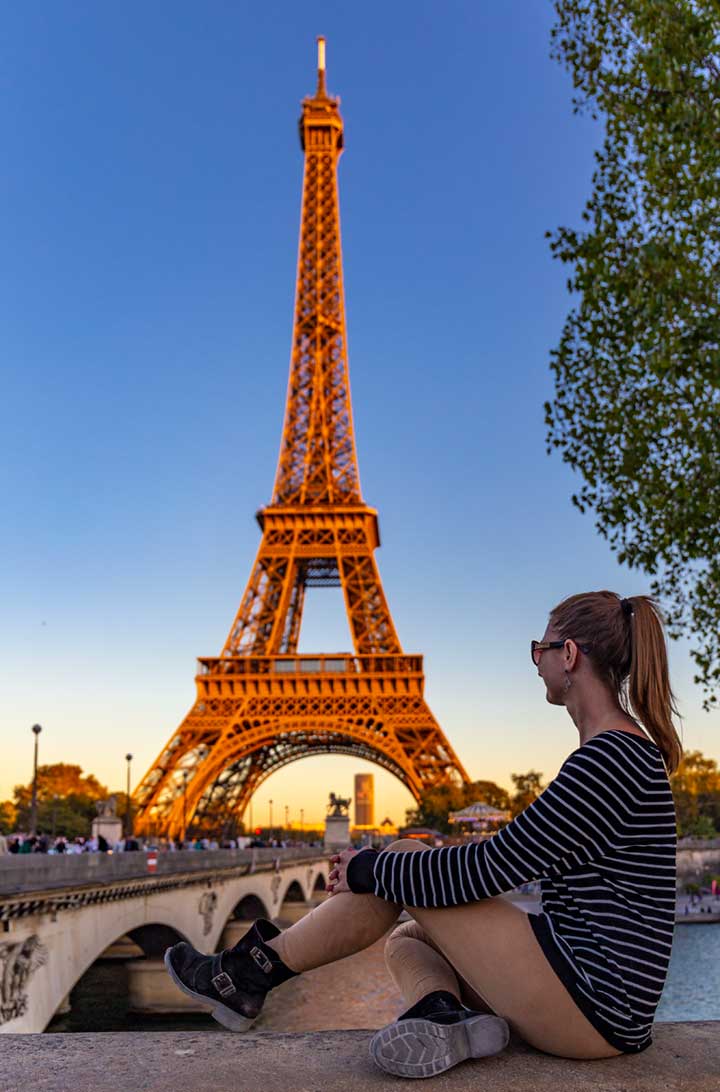 Mulher admira a Torre Eiffel iluminada pelo pôr do sol do outro lado do Rio Sena, em Paris