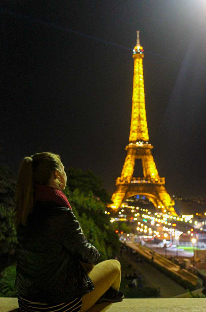 Mulher admira a Torre Eiffel iluminada à noite desde o Jardim do Trocadéro, em Paris