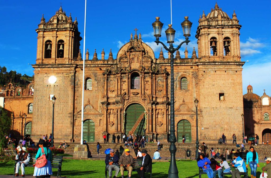 Pessoas sentam nos bancos da Plaza de Armas, em frente à Catedral de Cusco