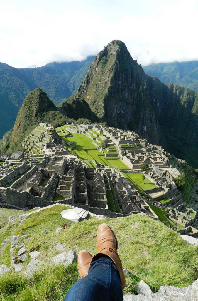 Pessoa mostra os pés diante das ruínas de Machu Picchu