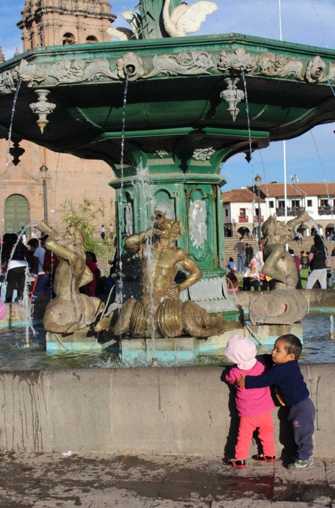 Casal de crianças se abraça na fonte da Plaza de Armas, em Cusco