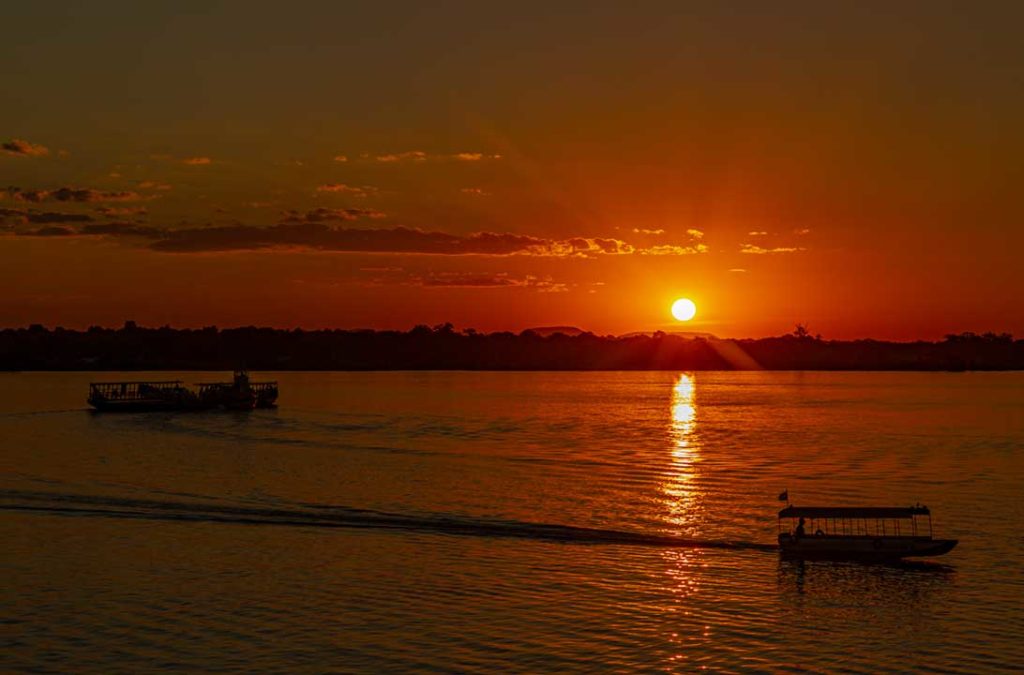 Barcos passam pelo Rio Tocantins enquanto o sol se põe ao fundo