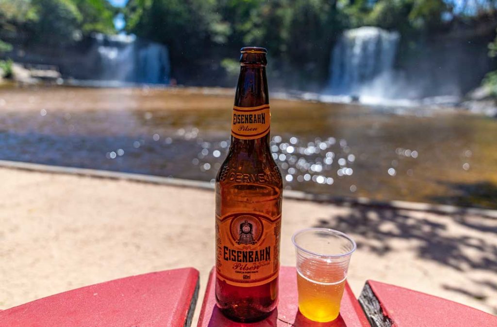 Garrafa e copo de cerveja sobre mesa de frente para as Cachoeiras do Itapecuru, atração da Chapada das Mesas