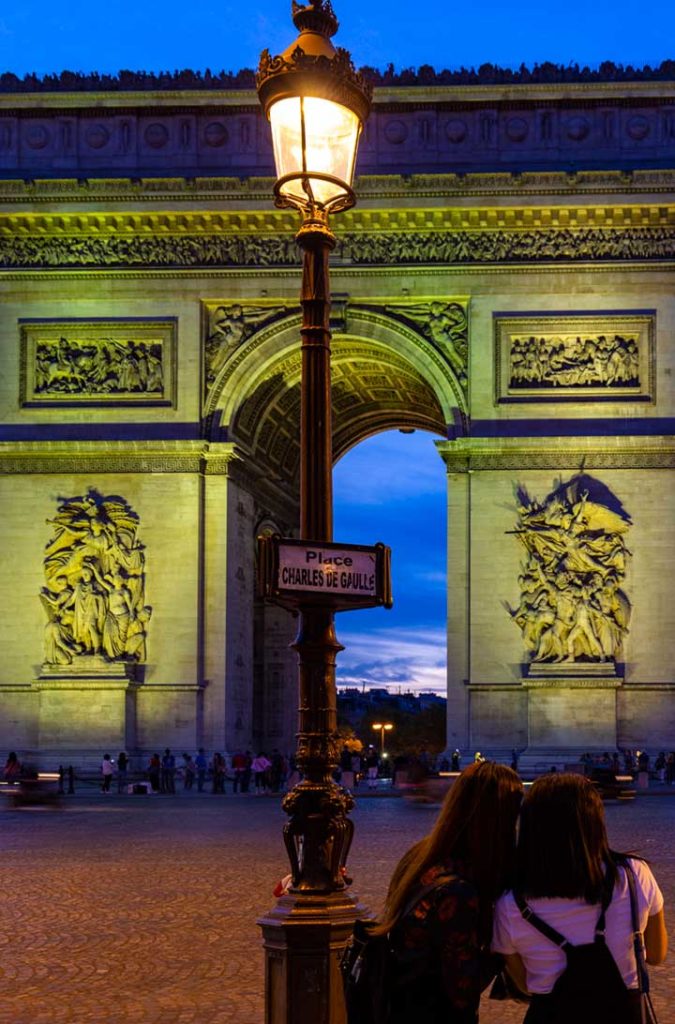 Mulheres observam o Arco do Triunfo, em Paris, ao anoitecer