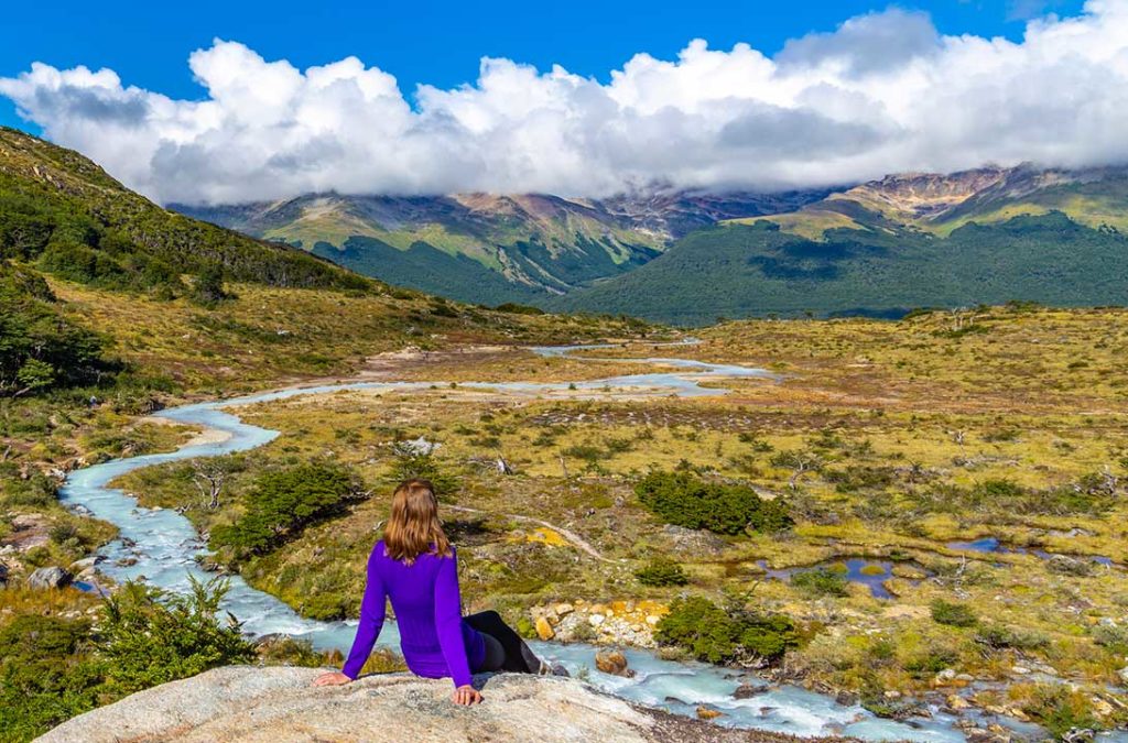 Mulher senta para admirar a vista na trilha da Laguna Esmeralda, em Ushuaia