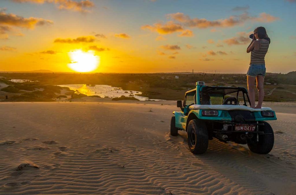 Mulher fotografa o pôr do sol em cima de um buggy nas dunas de Morro Branco, no Ceará (Brasil)