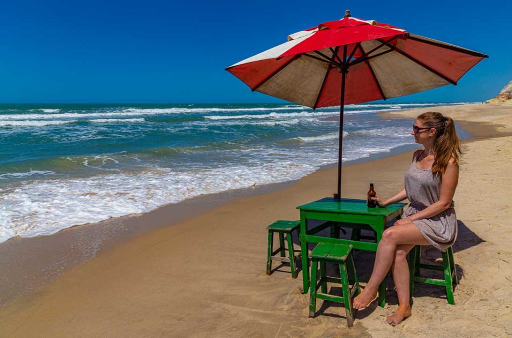 Mulher bebe cerveja em mesinha de bar na beira da Praia de Morro Branco