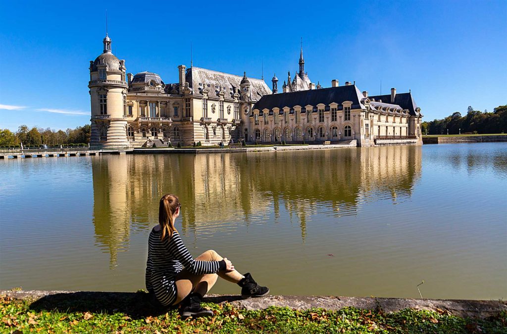 Mulher admira o Castelo de Chantilly do outro lado do lago