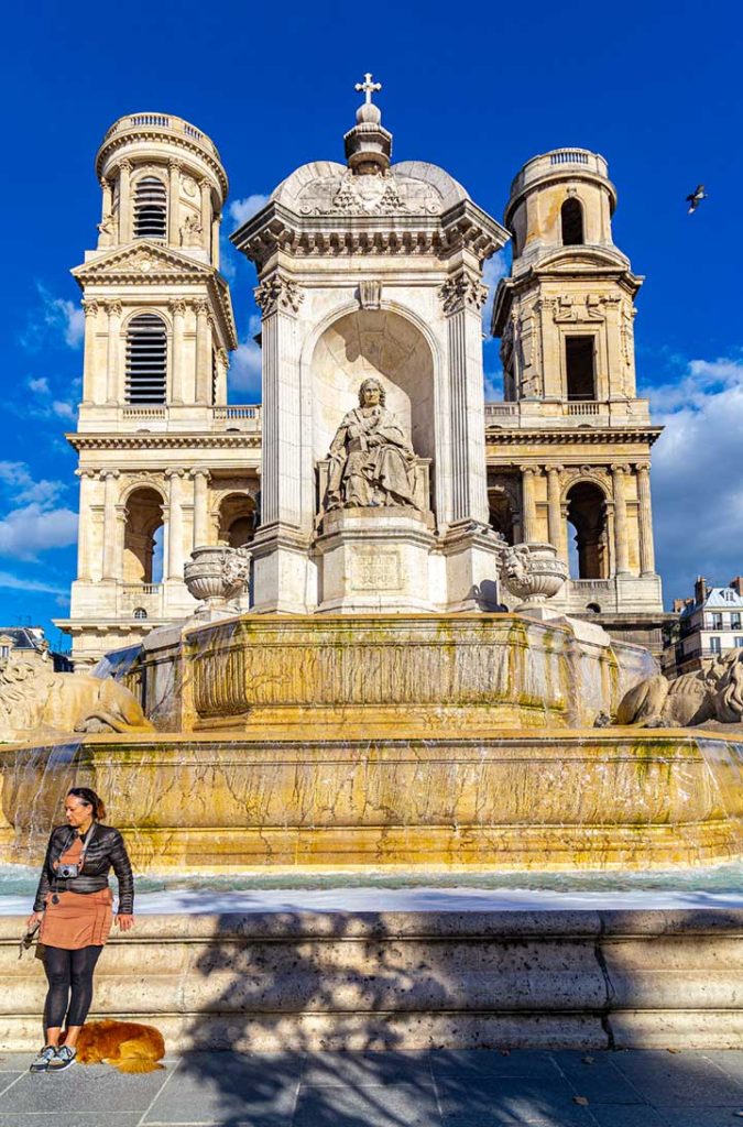 Mulher e cachorro em frente à fonte da Igreja de Saint-Sulpice, em Paris