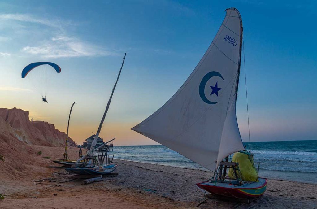 Parapente sobrevoa jangadas paradas na areia de Canoa Quebrada ao entardecer