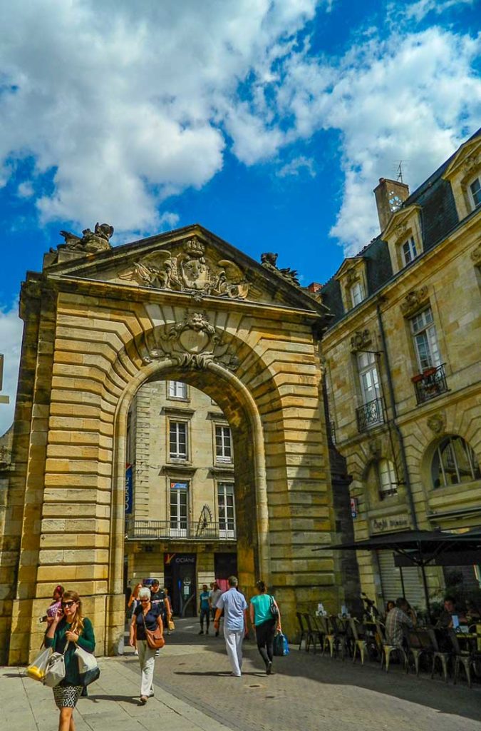 Pessoas atravessam o arco neoclássico da Porte Dijeaux, em Bordeaux