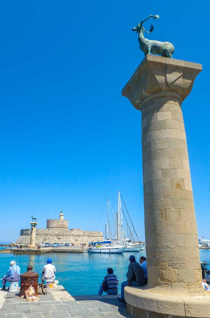 Homens pescam junto à coluna que simboliza o antigo local do Colosso de Rhodes