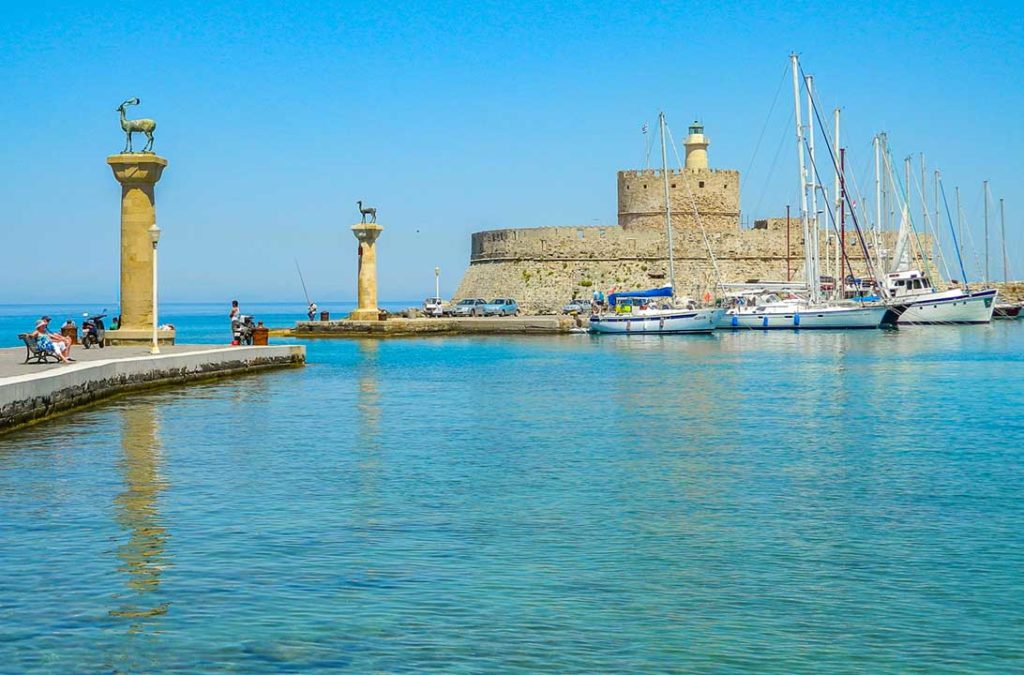 Vista do Porto de Mandraki, com as colunas do Colosso de Rhodes e a Fortaleza de Agios Nikolaos