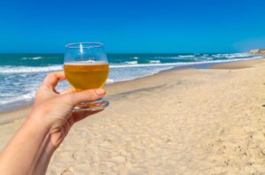 Pessoa segura copo de cerveja na beira da Praia das Fontes, em Beberibe (Ceará)